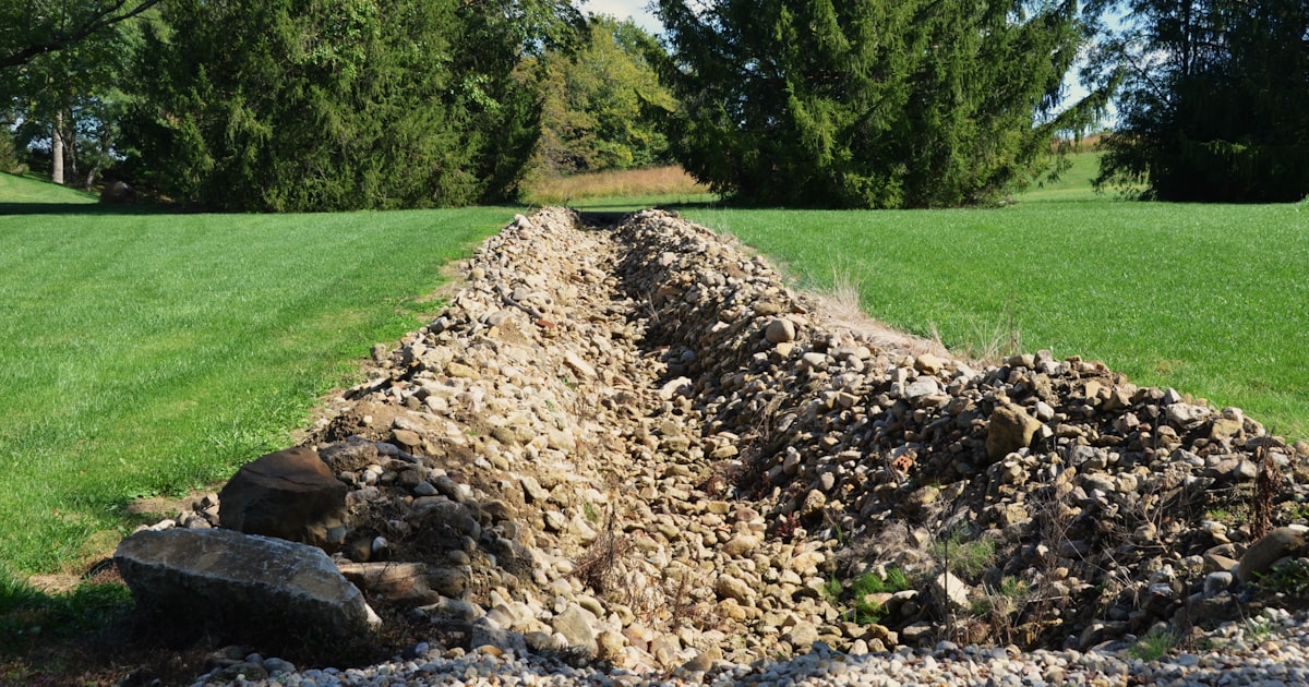French drain trench dug in a residential yard with gravel and drainage pipe visible during installation