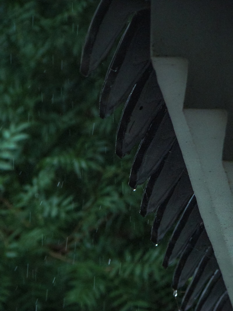 Raindrops falling from a dark roof edge showing water dripping without proper gutter direction, illustrating the need for drip edge or gutter apron flashing