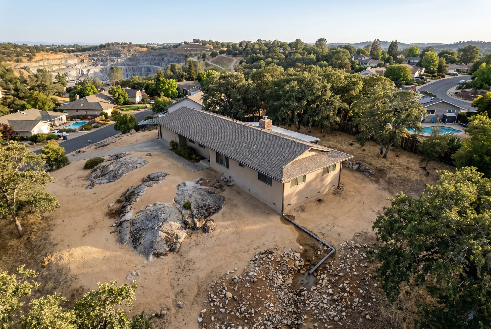 Aerial view of a Rocklin Quarry District home showing exposed granite bedrock outcrops, a downspout discharging onto rocky decomposed-granite soil, and the historic quarry visible in the background