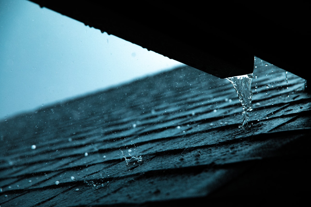 Close-up of a rain gutter mounted along a residential roofline where two roof planes converge at a valley, showing potential overflow point