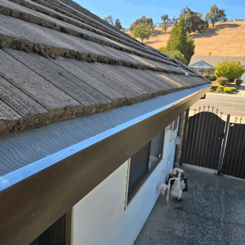 Bronze seamless gutter with micro-mesh guard on a concrete shake tile roof with dry foothills behind