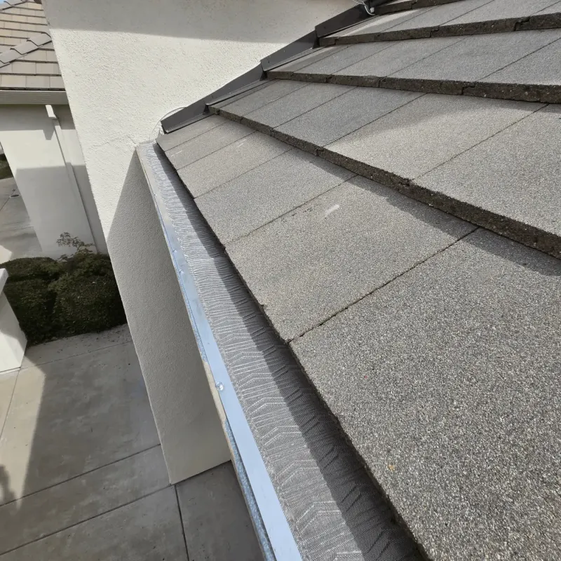Micro-mesh gutter guard along a grey flat tile roof where it meets a stucco wall