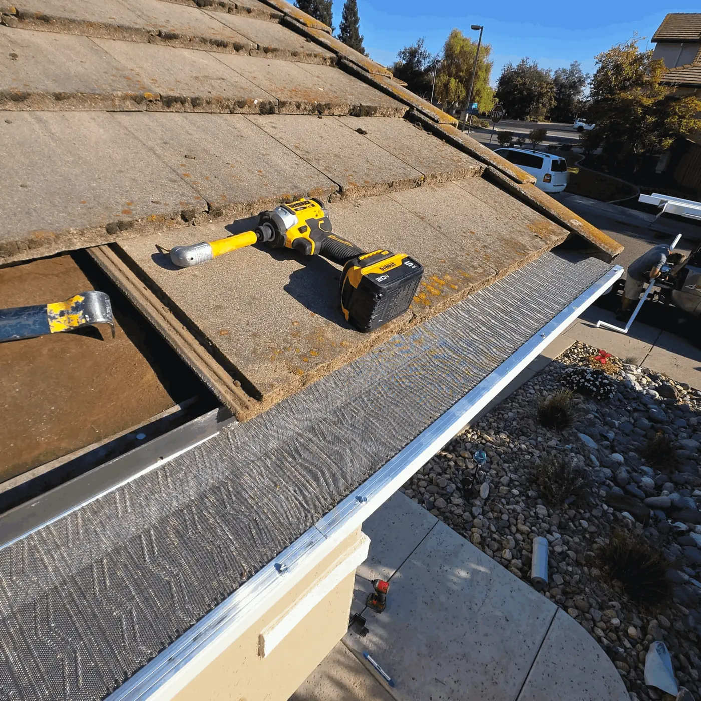 Impact driver on a concrete tile roof beside a freshly installed micro-mesh gutter guard