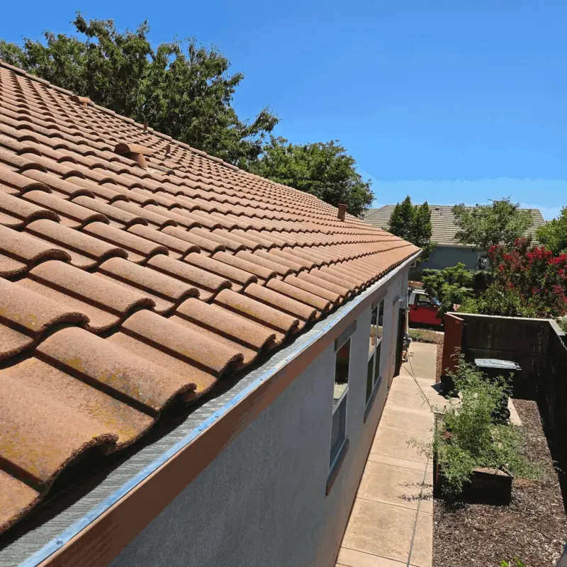 Gutter guard running the full side eave of a stucco home with a clay-color S-tile roof