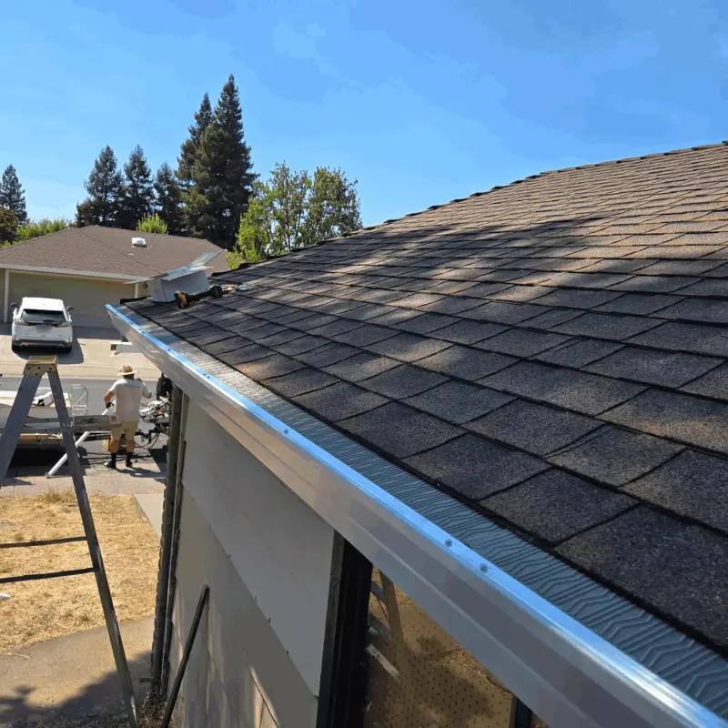 Finished gutter guard on a shingle roof while the crew works at the trailer in the driveway