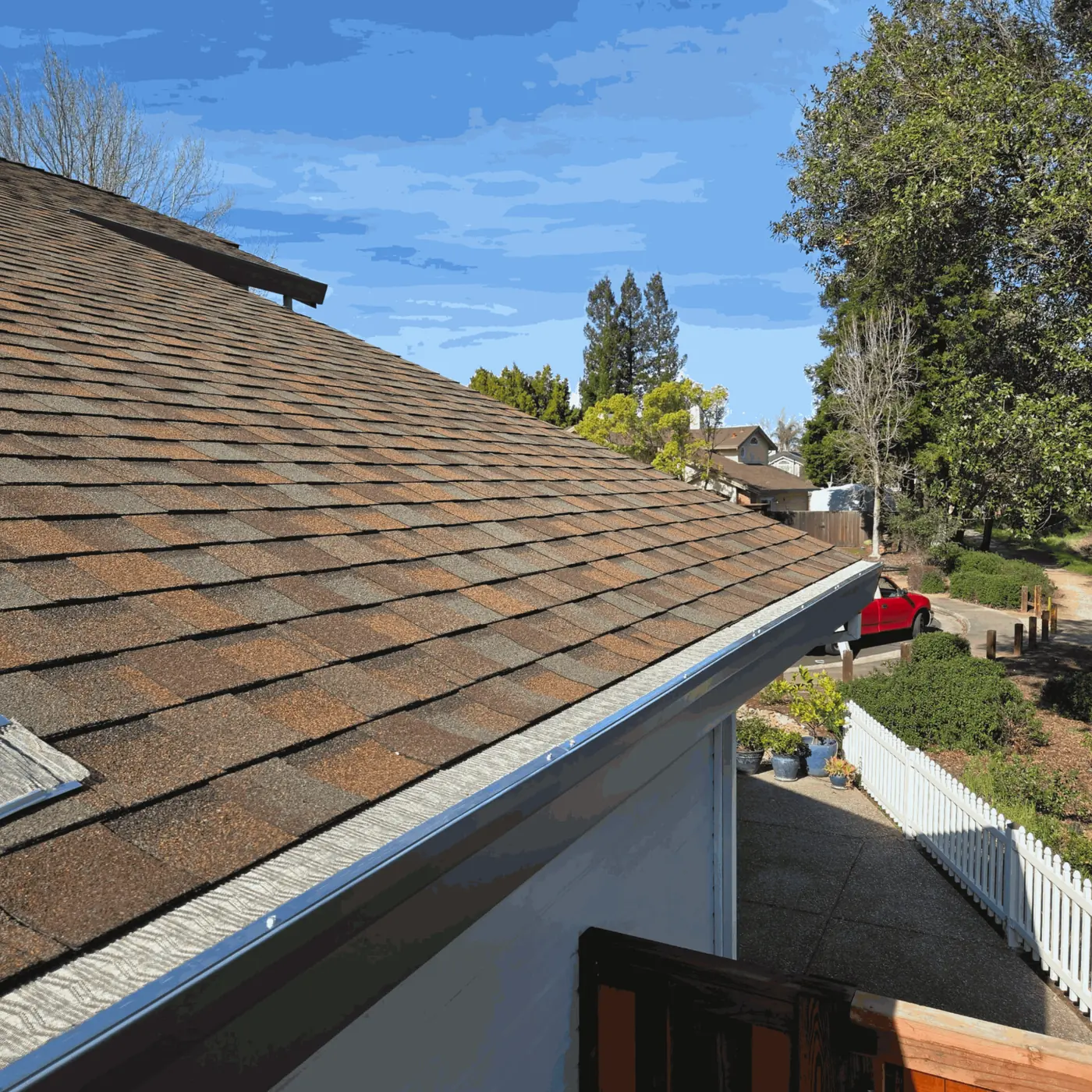 Gutter guard installed along a shingle roof eave above a side yard with a white picket fence
