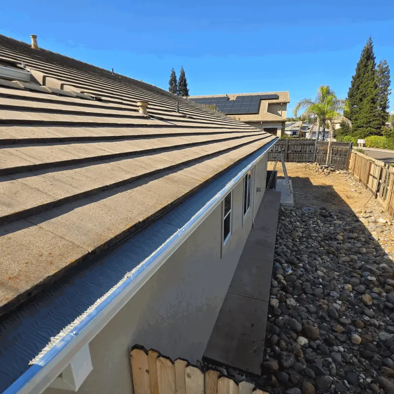 Long run of white seamless gutter with micro-mesh guard along a stucco home's flat tile roof