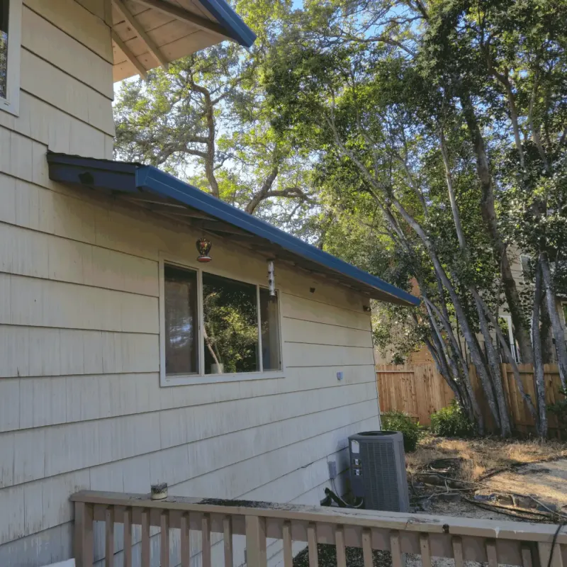 New dark blue seamless gutters on a sided home under a tree canopy