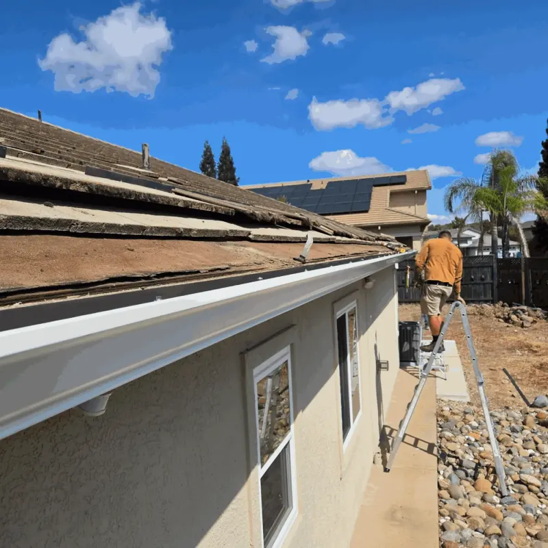 New white seamless gutter on a stucco home with an installer on a ladder further down the run