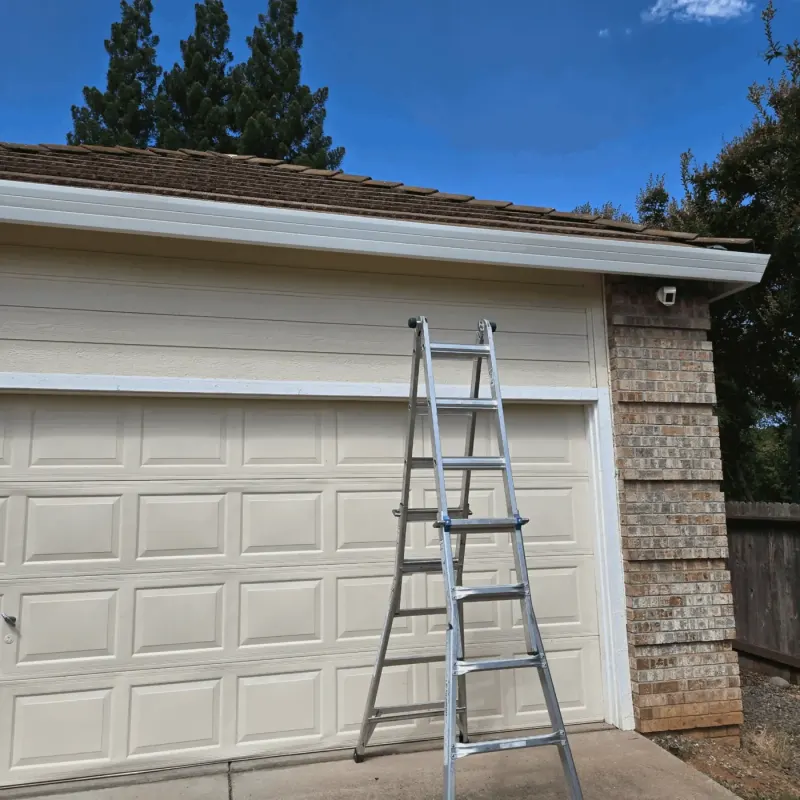 New white seamless gutter along a garage eave with a brick column and a ladder still set up