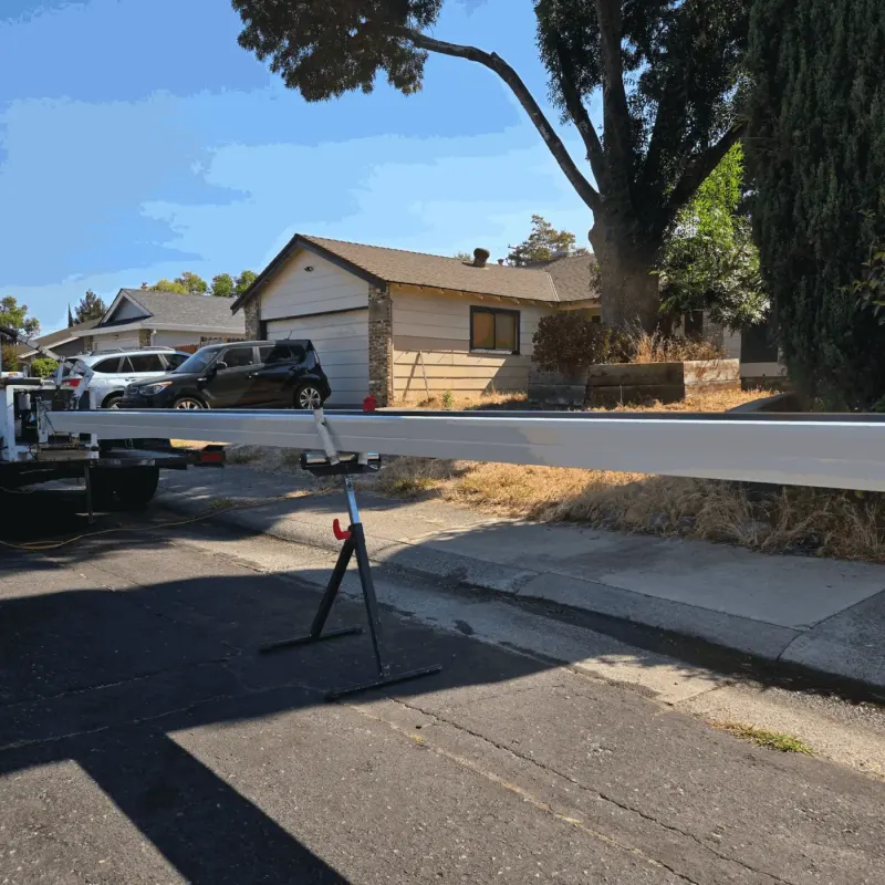 New white seamless gutter run fed from the forming machine onto a roller stand at the curb in front of a ranch home