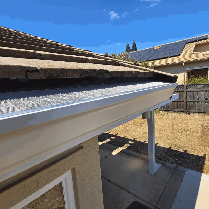 White seamless gutter with micro-mesh guard on a concrete tile roof above a backyard patio cover